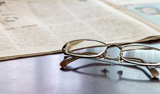 Lesebrille neben einer aufgeschlagenen Zeitung auf einem Tisch